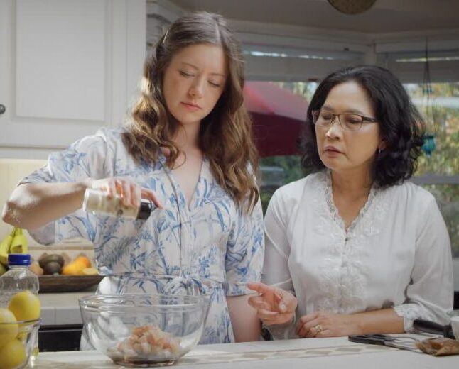 Two friends cooking together in a bright home kitchen, preparing food for a casual gathering.